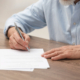 Senior man signing Last Will and Testament at wooden table, closeup