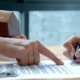 Hands signing a property agreement beside a set of keys and a wooden model house